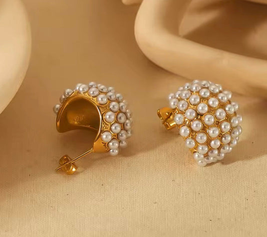 Gold earrings with pearl details on a beige surface