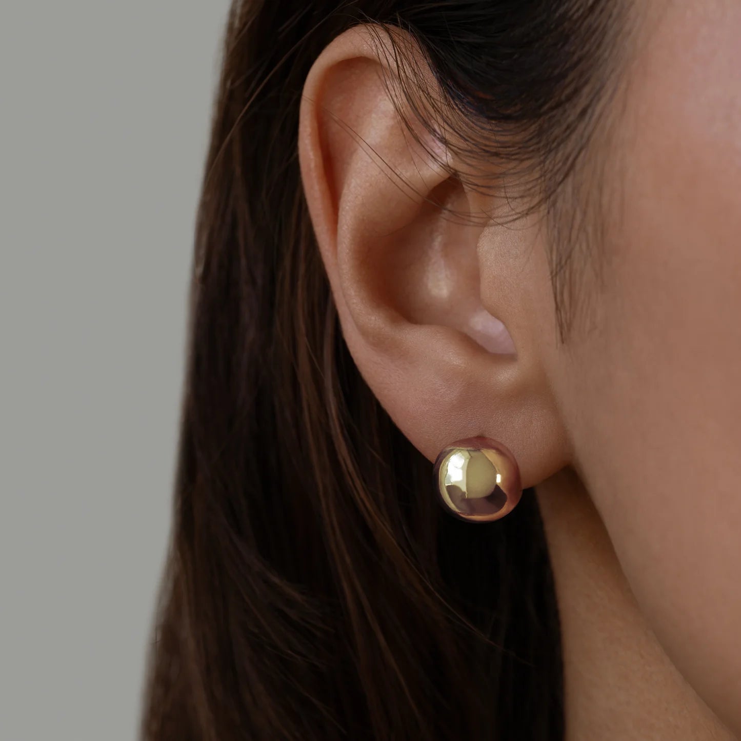 Close-up of an ear wearing a gold stud earring with a plain background